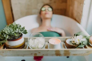 Estetista 2 Woman relaxing in a bathtub with a candle and plants, enjoying a serene spa experience.